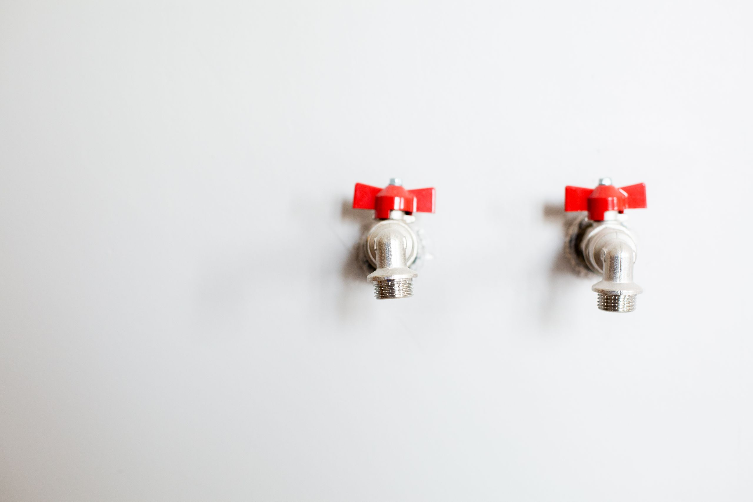 Two quarter-turn taps with red handles on a white wall, the kind of quick-closing valve that can cause water hammer